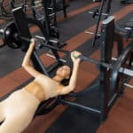 Woman pressing the barbell while lying down during training in the gym